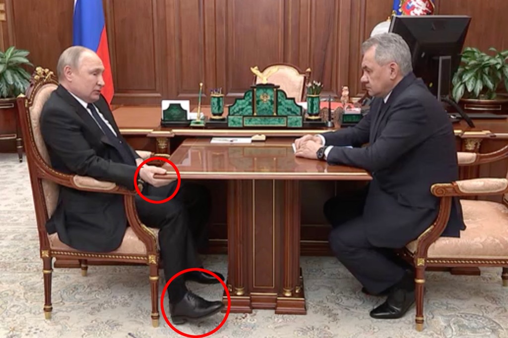 A bloated-looking Putin grabbing a table and twitching his feet.