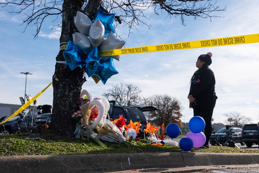 A person stands by a memorial to the Walmart victims, set up at a tree with balloons