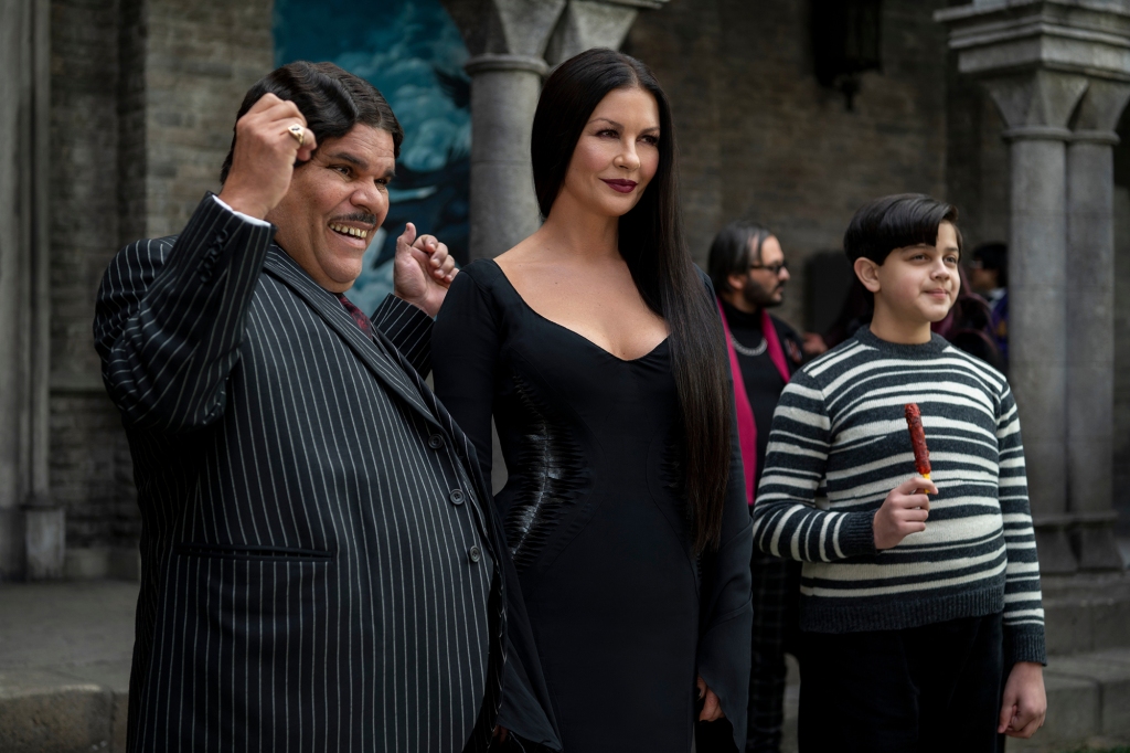 Luis Guzmán as Gomez Addams, Catherine Zeta-Jones as Morticia Addams, Issac Ordonez as Pugsley Addams in "Wednesday" stand and smile. 
