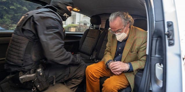 07 December 2022, Hessen, Frankfurt/Main: During a raid against so-called "Reich citizens", a hooded police officer sits in a police vehicle with the arrested Heinrich XIII Prince Reuß (r) after searching a house. 