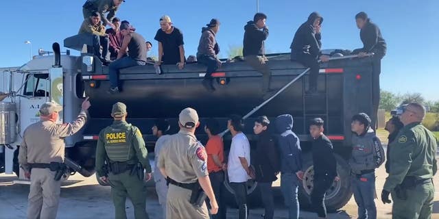 Migrants climb out of a dump truck. 