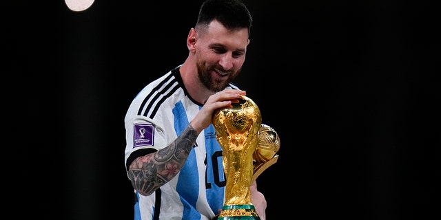 Argentina's Lionel Messi holds the Best Player of the Tournament trophy as he touches the World Cup trophy after the World Cup final soccer match between Argentina and France at the Lusail Stadium in Lusail, Qatar, Sunday, Dec. 18, 2022. 