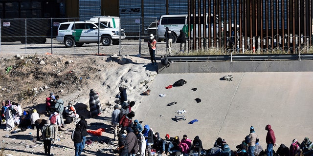 FILE - Migrants wait to cross the U.S.-Mexico border from Ciudad Juárez, Mexico, next to U.S. Border Patrol vehicles in El Paso, Texas, Wednesday, Dec. 14, 2022. A federal judge on Thursday temporarily blocked the Biden administration from ending a Trump-era policy requiring asylum-seekers to wait in Mexico for hearings in U.S. immigration court.