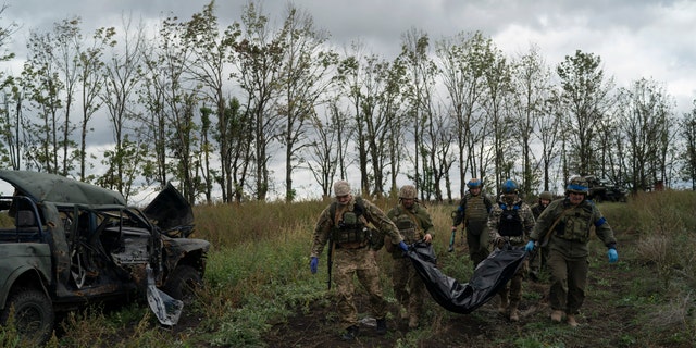 Ukrainian national guard servicemen carry a bag containing the body of a Ukrainian soldier in an area near the border with Russia, in Kharkiv region, Ukraine, Monday, Sept. 19, 2022. 