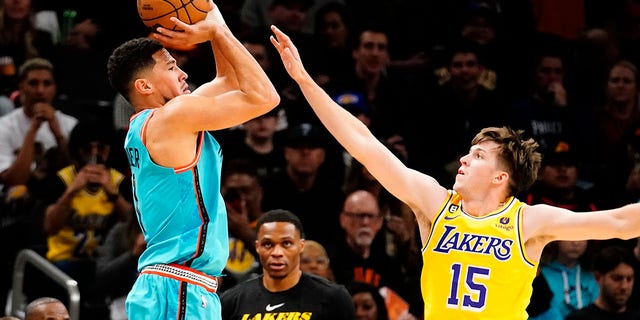 Phoenix Suns' Devin Booker shoots a three pointer against Los Angeles Lakers' Austin Reaves (15) during the first half of an NBA basketball game in Phoenix, Tuesday, Nov. 22, 2022. 