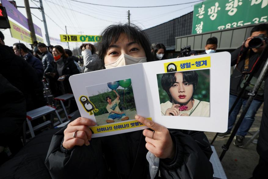 A woman holds up a small booklet as she waits for the arrival of Jin, the oldest member of the K-pop band BTS, in Yeoncheon on Dec. 13, 2022.