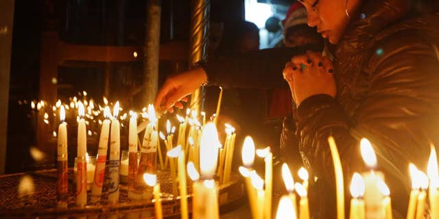 A Christian worshipper prays after lighting a candle on Christmas Eve at the Church of the Nativity, built atop the site where Christians believe Jesus Christ was born, in the West Bank City of Bethlehem, Saturday, Dec. 24, 2016.