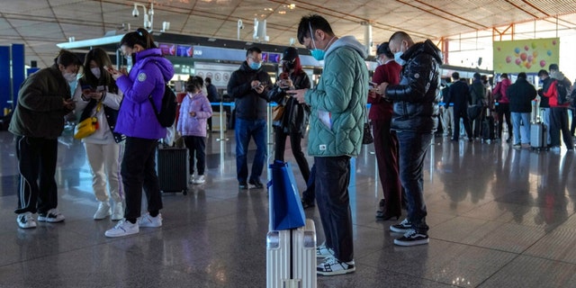 Masked travelers use their smartphones to fill in their health declaration after checking in at the international flight check in counter at the Beijing Capital International Airport in Beijing, Thursday, Dec. 29, 2022. 