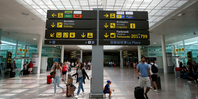 People walk under a sign at Barcelona's El Prat airport in Spain pn Aug. 4, 2017.