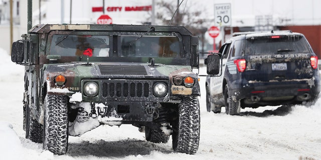 A National Guard truck drives past a police cruiser on a snowy street in Buffalo, New York, on Tuesday, Dec. 27, 2022. 