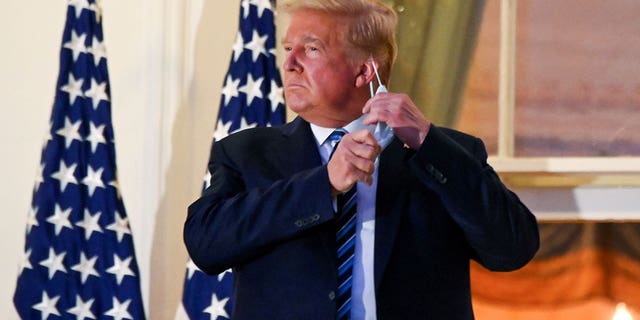 Then-President Donald Trump pulls off his protective face mask as he poses atop the Truman Balcony of the White House after returning from being hospitalized at Walter Reed Medical Center for coronavirus disease (COVID-19) treatment, in Washington, U.S. October 5, 2020.