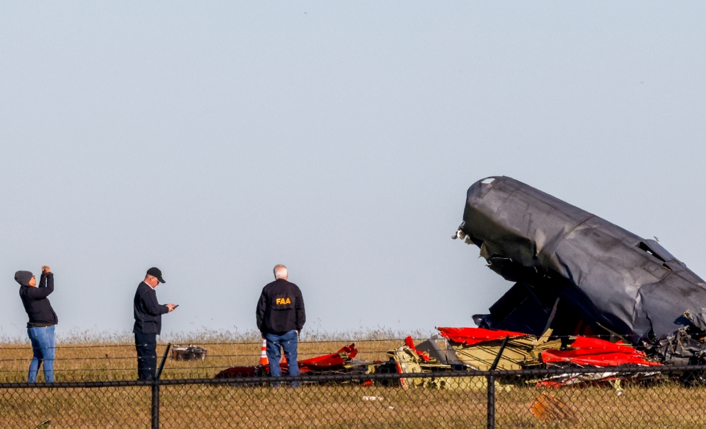 Officials, including those from the Federal Aviation Administration, survey damage from the crash of a Boeing B-17 Flying Fortress and a Bell P-63 Kingcobra at Dallas Executive Airport.