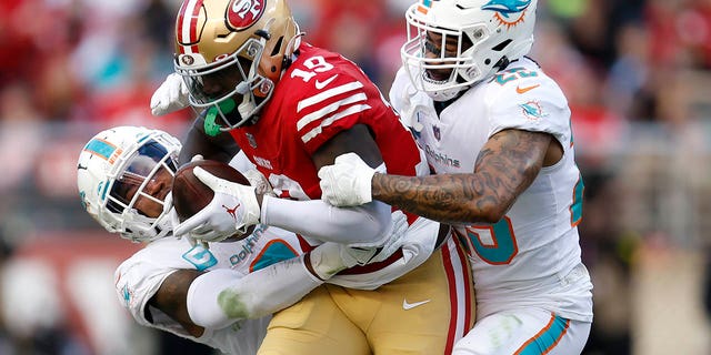 San Francisco 49ers wide receiver Deebo Samuel, #19, runs between Miami Dolphins safety Jevon Holland, left, and cornerback Xavien Howard during the second half of an NFL football game in Santa Clara, California, Sunday, Dec. 4, 2022. 