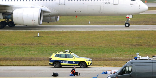 The last of four climate activists sits with his hand glued to the feeder road of a runway at Franz-Josef-Strauss Airport in Munich, Germany, Thursday, Dec. 8, 2022. 