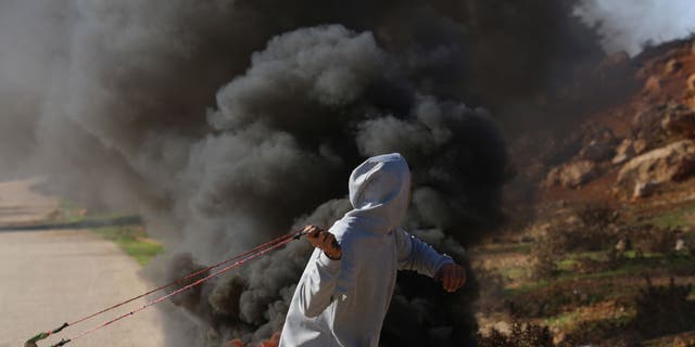 A Palestinian man uses a catapult against Israeli troops during a protest against new construction at Jewish settlements in the West Bank. 