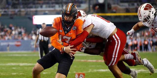 Quarterback Garret Rangel, #13 of the Oklahoma State Cowboys, fumbles the ball out of bounds after being hit by cornerback Avyonne Jones, #8 of the Wisconsin Badgers, during the second half of the Guaranteed Rate Bowl at Chase Field on Dec. 27, 2022 in Phoenix.