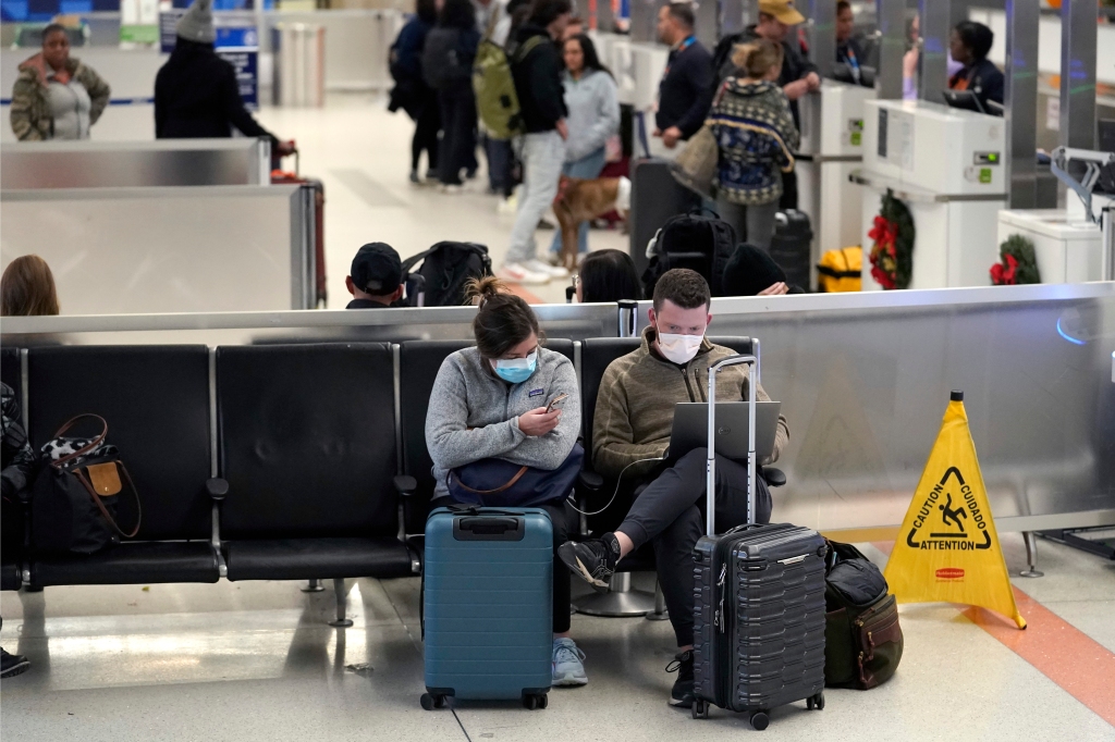 Travelers sit near their luggage near a check-in area on Dec. 20, 2022, in Terminal C at Boston Logan International Airport.