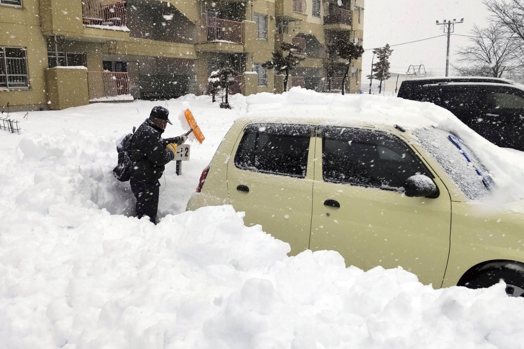 A resident shovels snow off around a car at a parking lot in Kitami city Hokkaido prefecture, northern Japan.