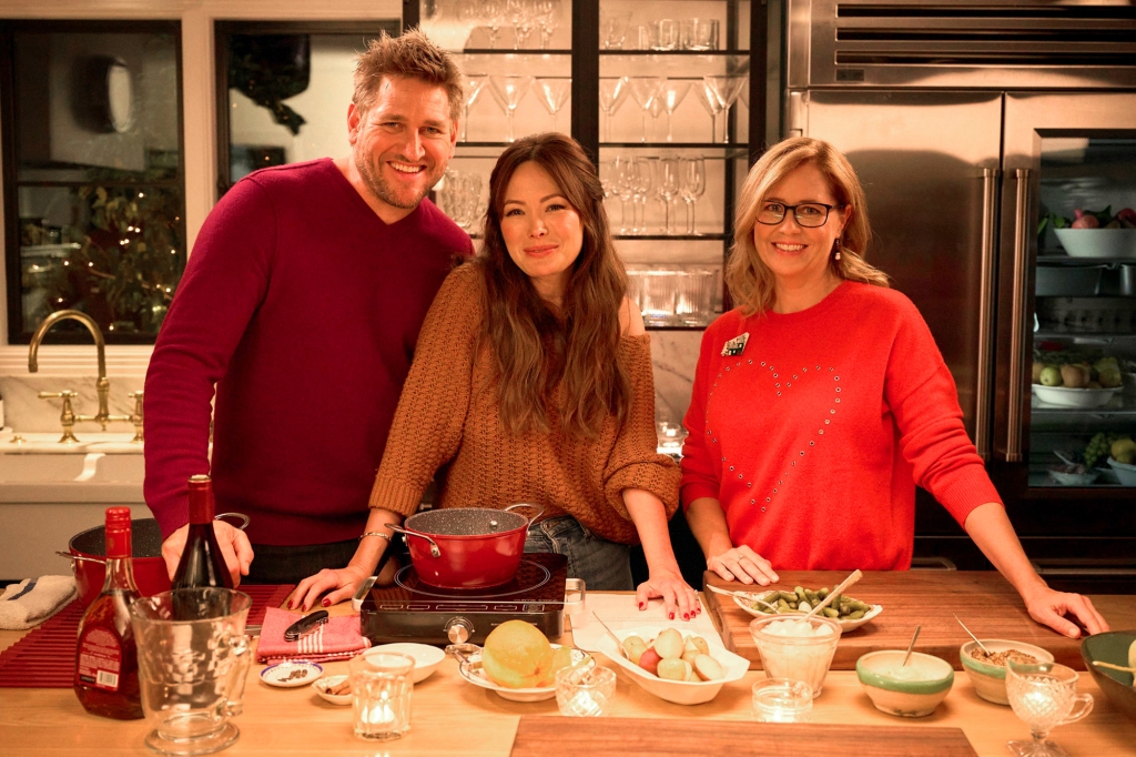 Curtis Stone, Lindsay Price-Stone and Jenna Fischer are posing in front of a table laden with food. Curtis and Jenna are wearing red shirts.