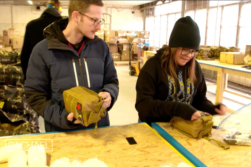 Photo of Rachael Ray and a man standing side-by-side in a warhouse. It's cold -- Rachael is wearing as big sweater and a winter cap -- and they're packing supplies.