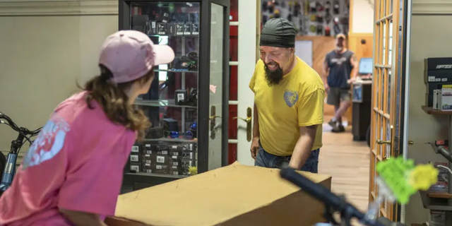 Steven Pringle, owner of Build a Bicycle - Bicycle Therapy, and his girlfriend Lindsey Gagne, carry in a box with a new electric bicycle at his shop in Kingsford, Mich., on Friday, July 29, 2022.