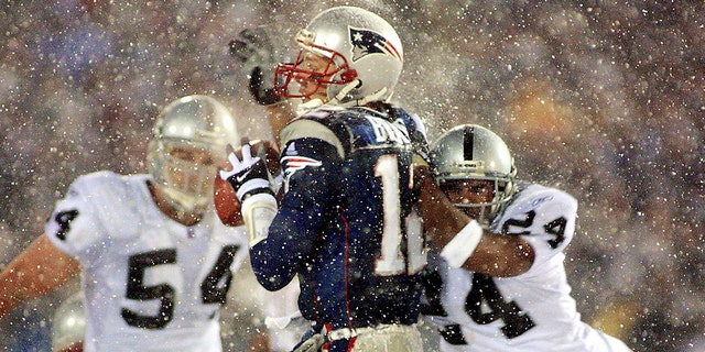 New England Patriots quarterback Tom Brady takes a hit from Charles Woodson of the Oakland Raiders on a pass attempt in the last two minutes of the game in their AFC playoff January 19, 2002 in Foxboro, Massachusetts.