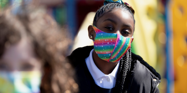 Students play outside at recess wearing a rainbow mask.