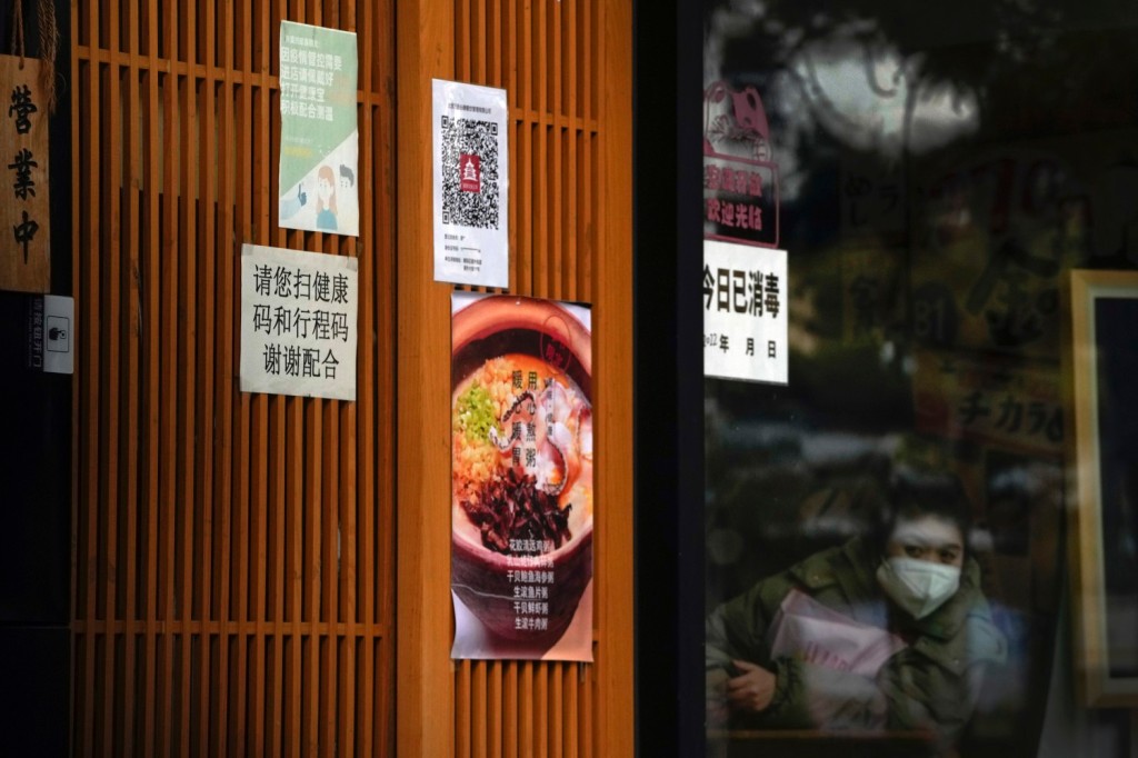 A masked worker looks out from a restaurant as its entrance door displays a health check QR code and a notice that reads "Please scan your health QR code and travel code, thank you for your cooperation" in Beijing on Dec. 12, 2022. 