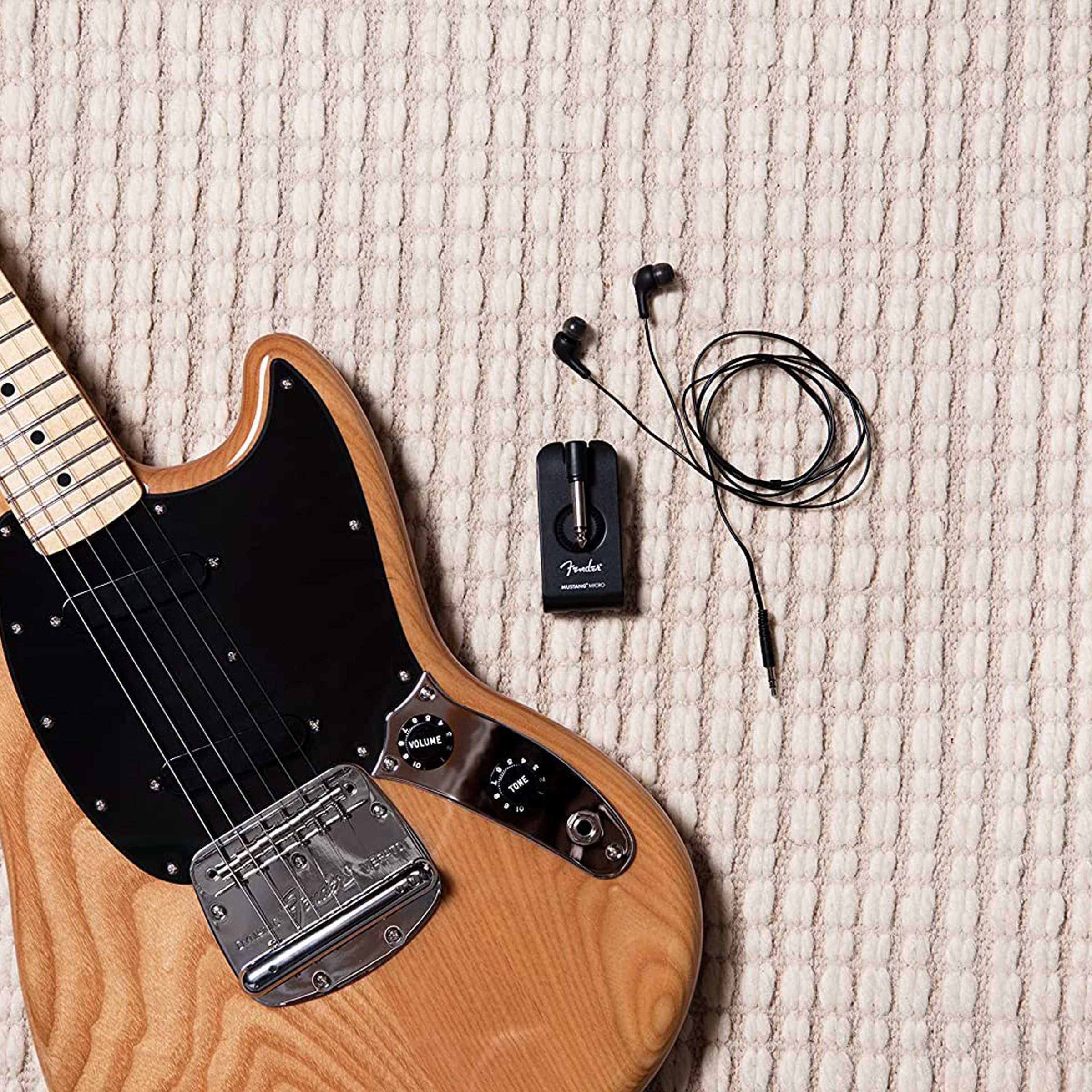 Small headphone amplifier to the left of an electric guitar.