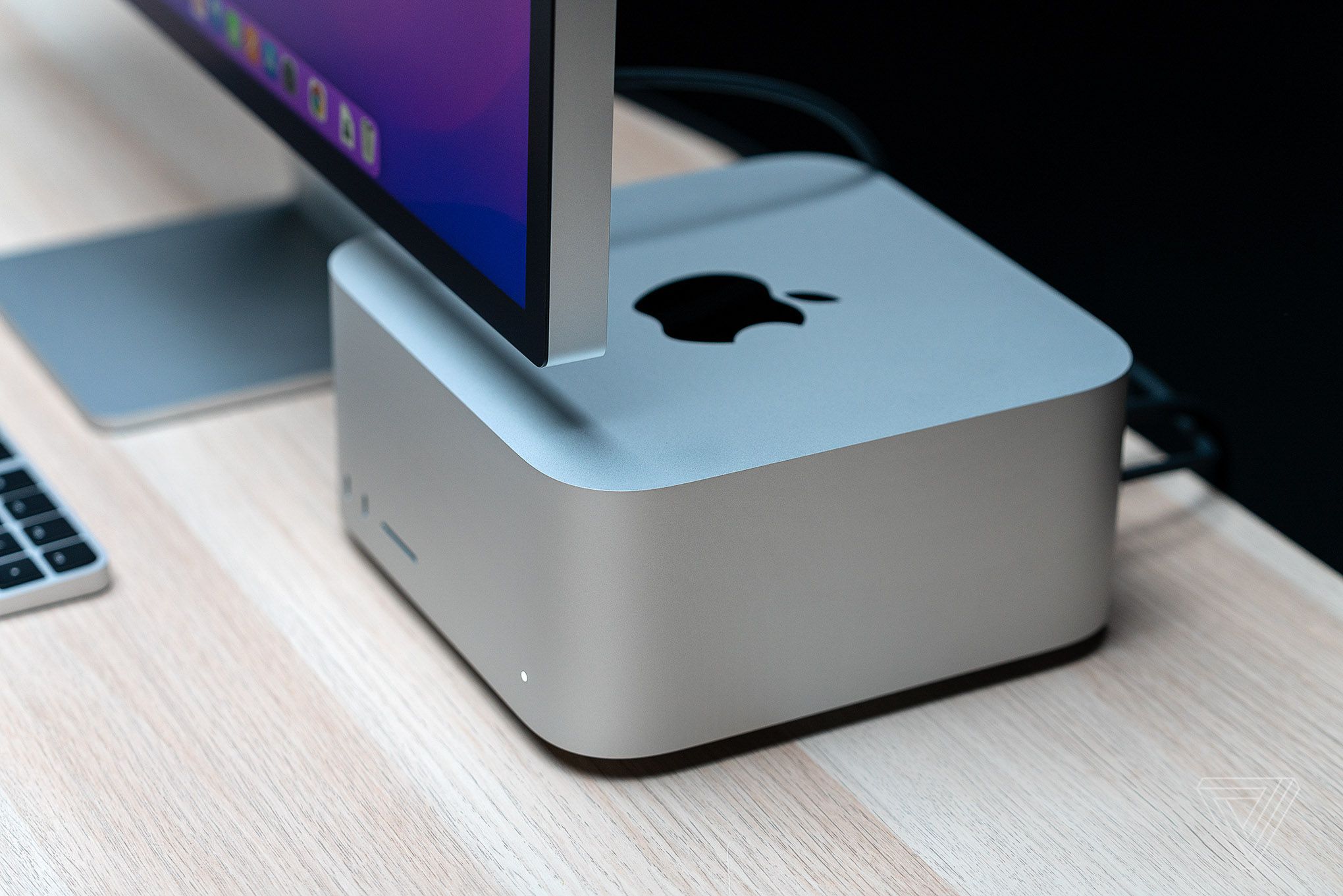 The Mac Studio beneath the Studio Display on a wooden table.