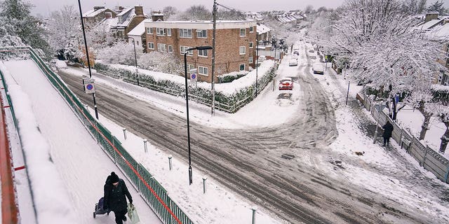 A woman pulls a shopping trolley, in a snow covered residential area in Leytonstone, in London, Monday, Dec. 12, 2022. Snow and ice have swept across parts of the UK, with cold wintry conditions set to continue for days. 