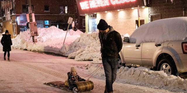 TOPSHOT - A family walks past Cameron's 24 Hour Store in Buffalo, New York, on December 26, 2022. - Emergency crews in New York were scrambling on December 26, 2022, to rescue marooned residents from what authorities called the "blizzard of the century," a relentless storm that has left at least 25 dead in the state and is causing US Christmas travel chaos. (Photo by Joed Viera / AFP) (Photo by JOED VIERA/AFP via Getty Images)