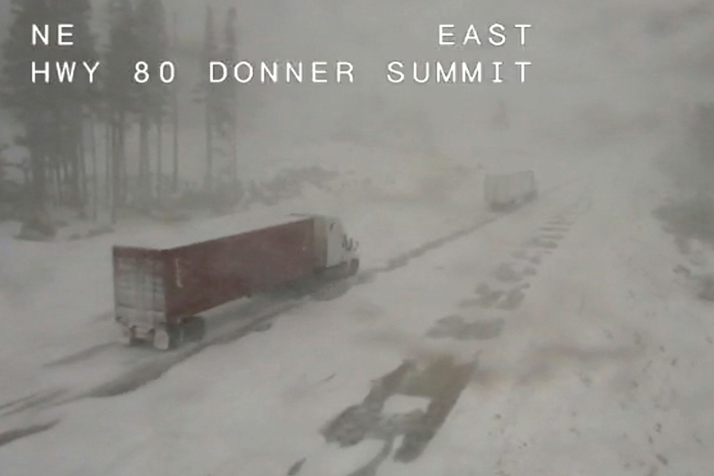 A pair of trucks make their way through the snowy conditions along Interstate 80 at Donner Summit, California on Dec. 1, 2022.