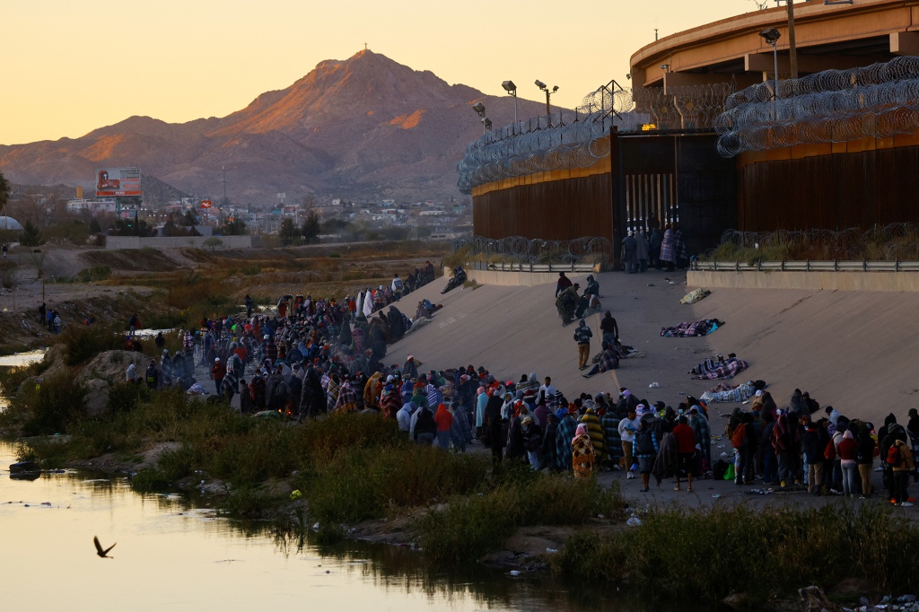 Migrants queue near the border wall after crossing the Rio Bravo river.