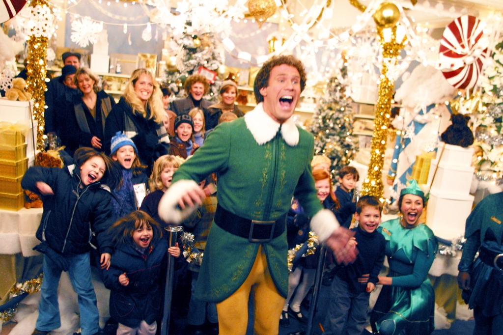 Will Ferrell in an elf outfit shouting and smiling surrounded by people. 