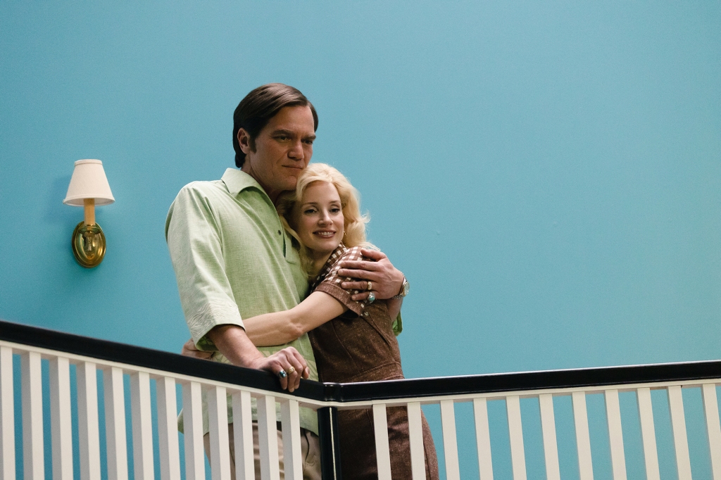 Michael Shannon and Jessica Chastain as George Jones and Tammy Wynette in "George & Tammy." They're standing near a staircase bannister and George had his arm around Tammy. There's a blue wall behind them with a light fixture hanging on it. It looks like it's the 1970s; Tammy has long blond hair.