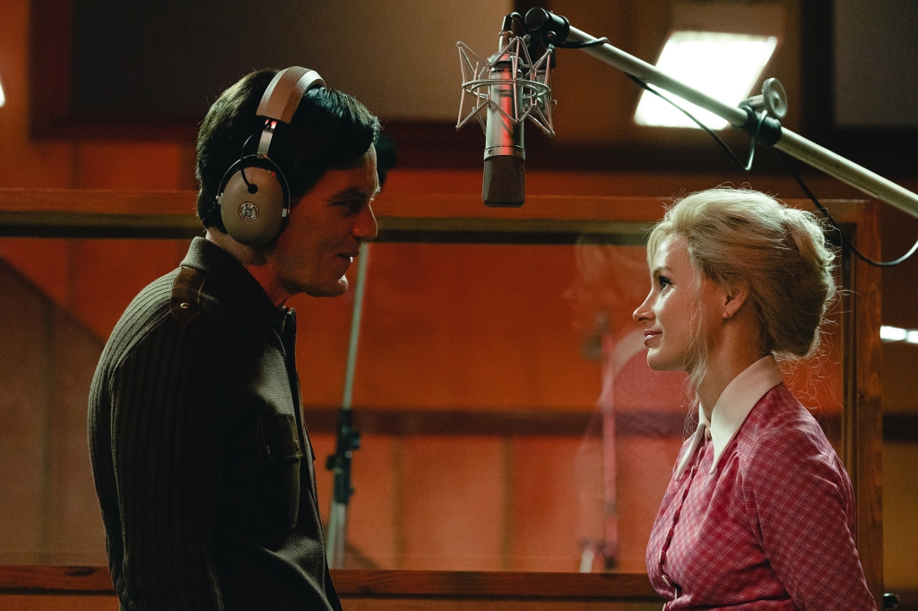 Michael Shannon and Jessica Chastain as George and Tammy recording together in Quonset Hut Studio in the 1970s. They're facing each other; George is wearing headphones and smiling at Tammy, who has a smile on her face and is wearing a red shirt with a white collar.