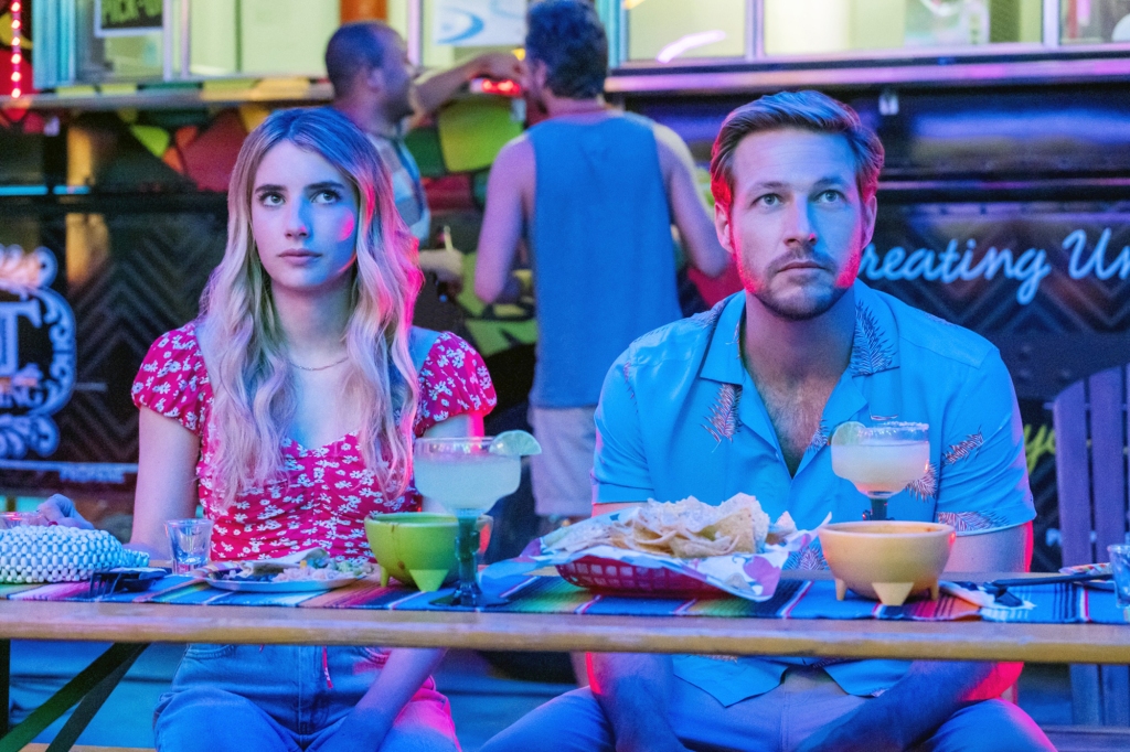 Emma Roberts and Luke Bracey in "Holidate" sitting next to each other eating food. 
