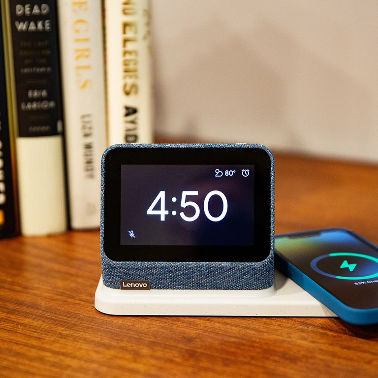 The Lenovo Smart Clock 2 displaying the time while a phone wirelessly charges on its dock.