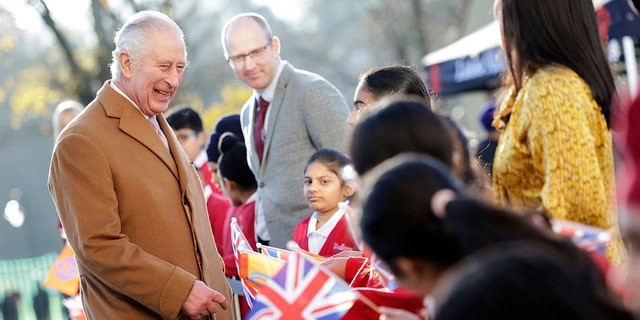 Britain's King Charles III smiles as he speaks with local school children waving flags during a visit to the newly built Guru Nanak Gurdwara, in Luton, England, Tuesday, Dec. 6, 2022. 