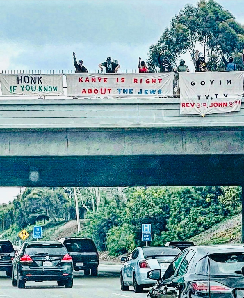 

Photos  show a small group of demonstrators with their arms raised in what appears to be the Nazi salute behind banners reading, “honk if you know” alongside “Kanye is right about the Jews.”