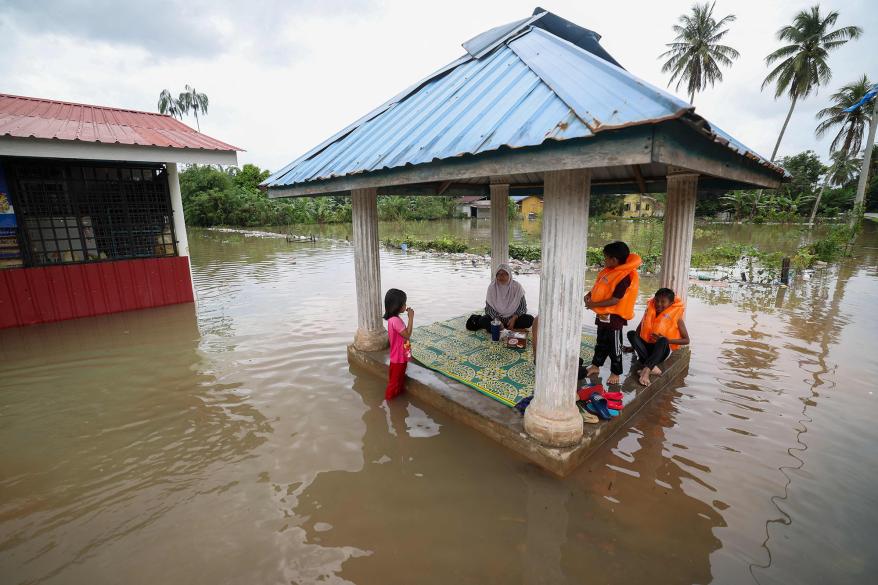 A family sits in a pergola surrounded by floodwaters in Pasir Mas in Malaysia's northern Kelantan state on Dec. 21, 2022.