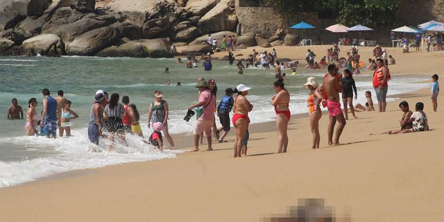 Tourists enjoy the beach near one of three bodies with signs of torture that were washed ashore by the sea, according to local media, at Icacos beach, in Acapulco, Mexico Nov. 12, 2022. 