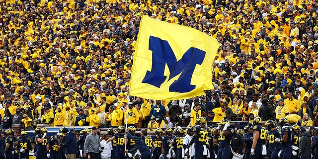 A cheerleader runs a Michigan Wolverines flag up the field after a touchdown during a game against the Penn State Nittany Lions at Michigan Stadium on October 15, 2022 in Ann Arbor, Michigan. 