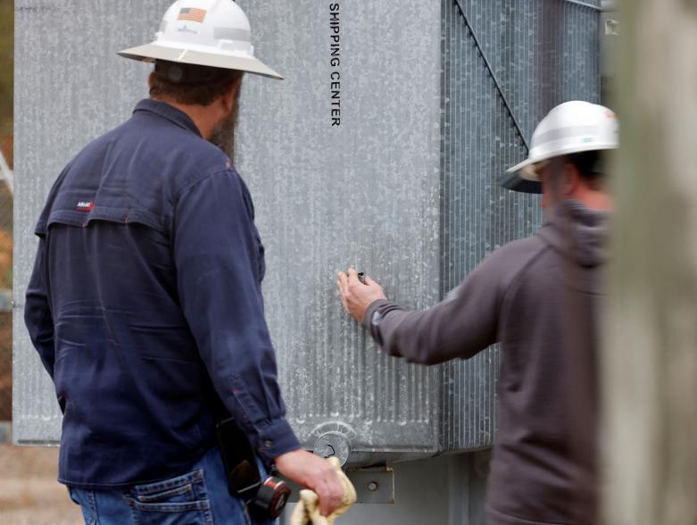 Duke Energy workers inspect one of the bullet holes that hit an electrical substation.