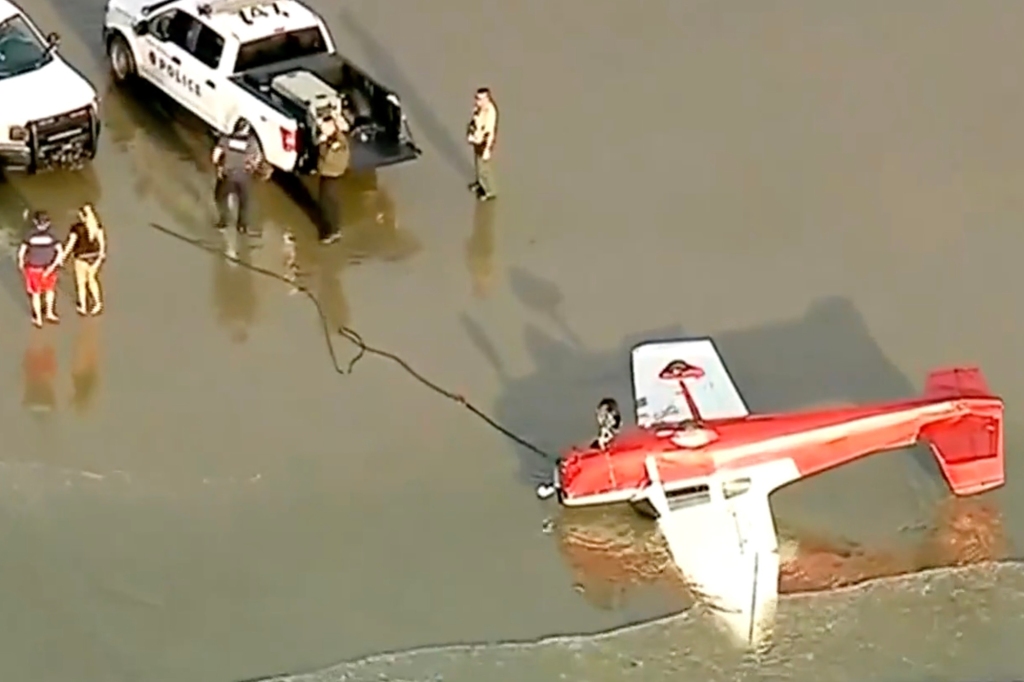 Crashed plane upside-down in the surf as responders arrive.
