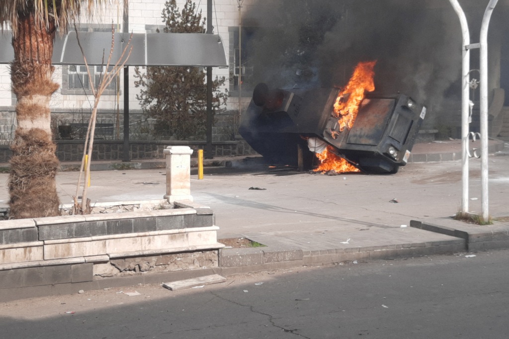 A vehicle burns as people take part in a protest.