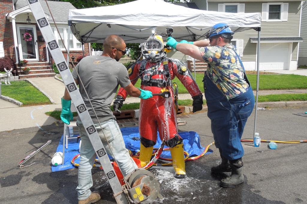 Donn Gann standing in a diving suit, while men around him sanitize it. 