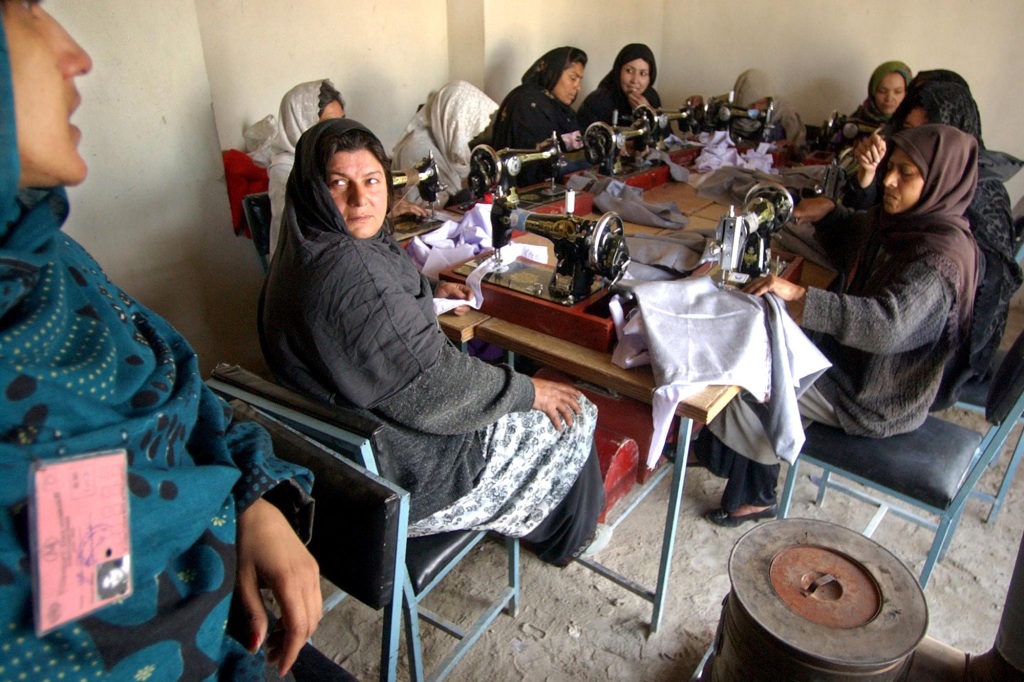 Women, whose husband's aren't able to work, chat while they sew children's clothing at a factory