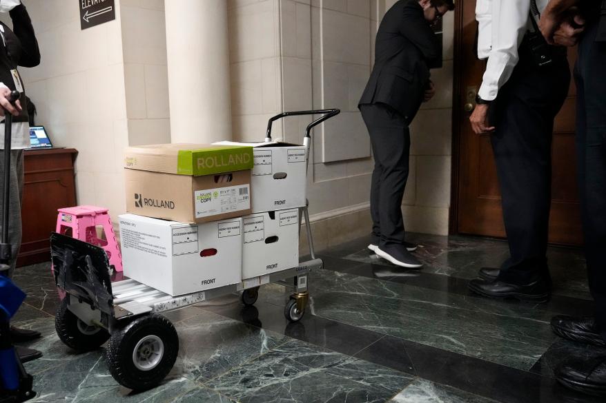 A picture of staff members move boxes of documents from the hearing room to the office of the House Ways and Means Committee.